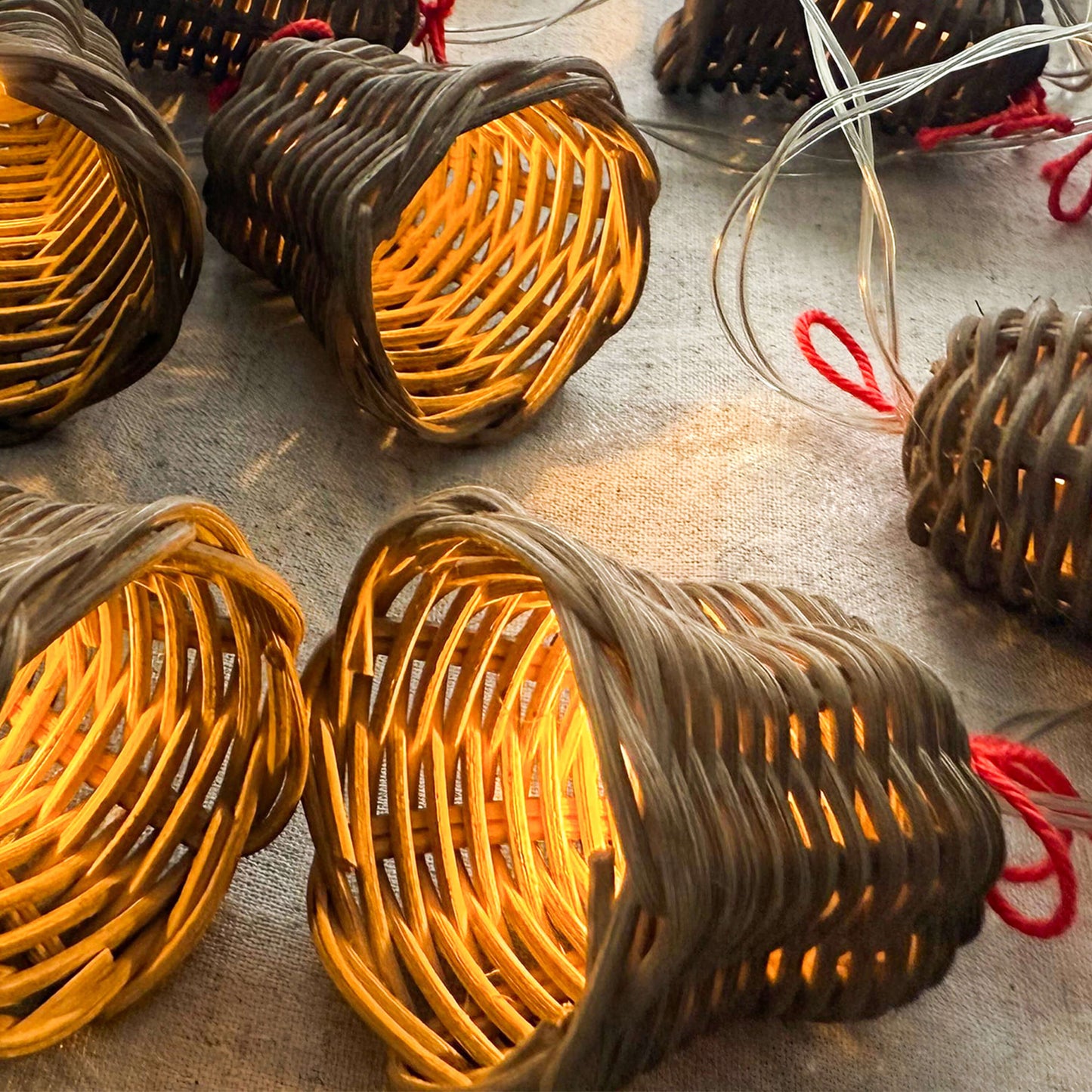 20 adet el yapımı rattan çan başlıklı LED ışık zinciri, kırmızı ip detaylı, beyaz zeminde dağınık konumda – pille çalışan dekoratif boho aydınlatma