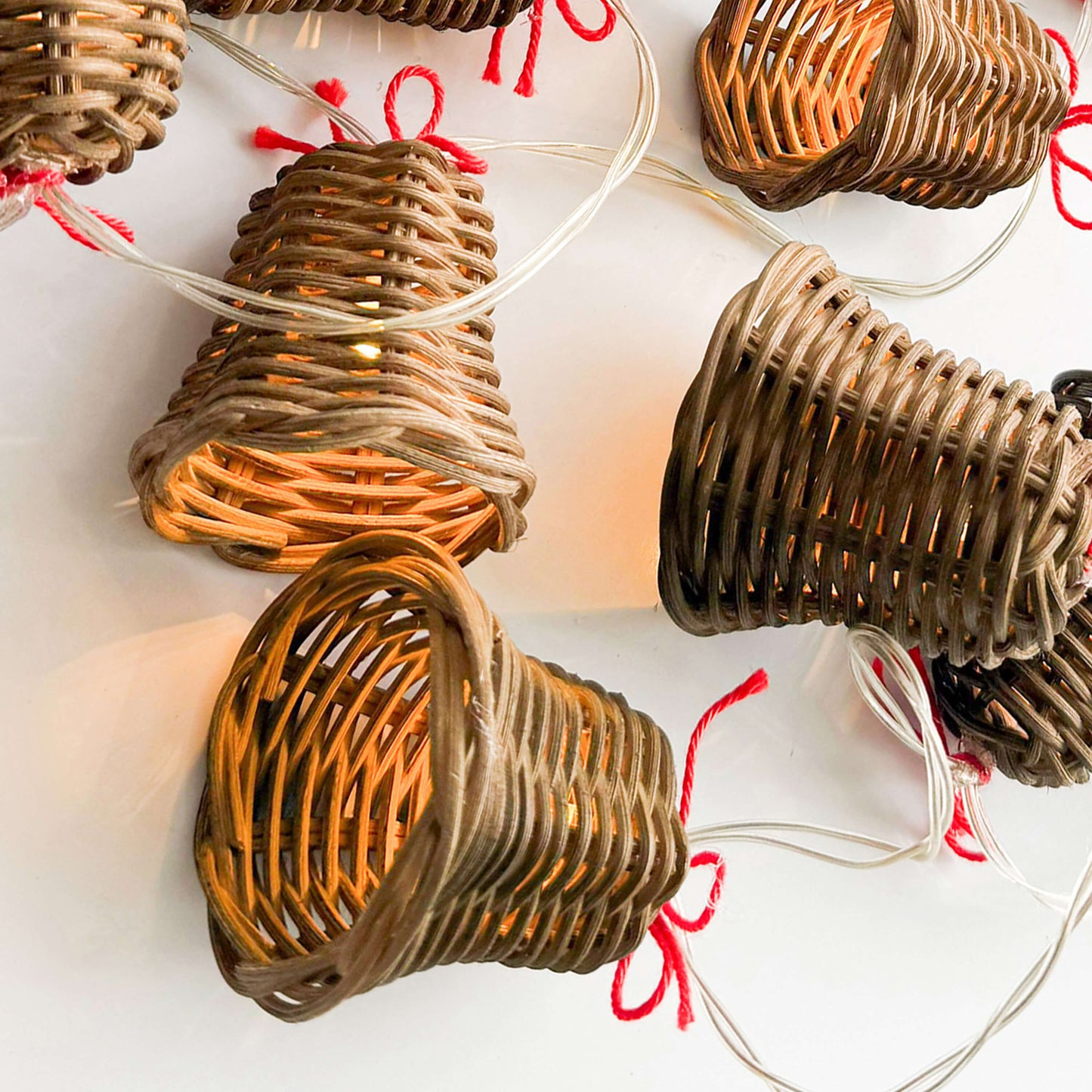 20 adet el yapımı rattan çan başlıklı LED ışık zinciri, kırmızı ip detaylı, beyaz zeminde dağınık konumda – pille çalışan dekoratif boho aydınlatma