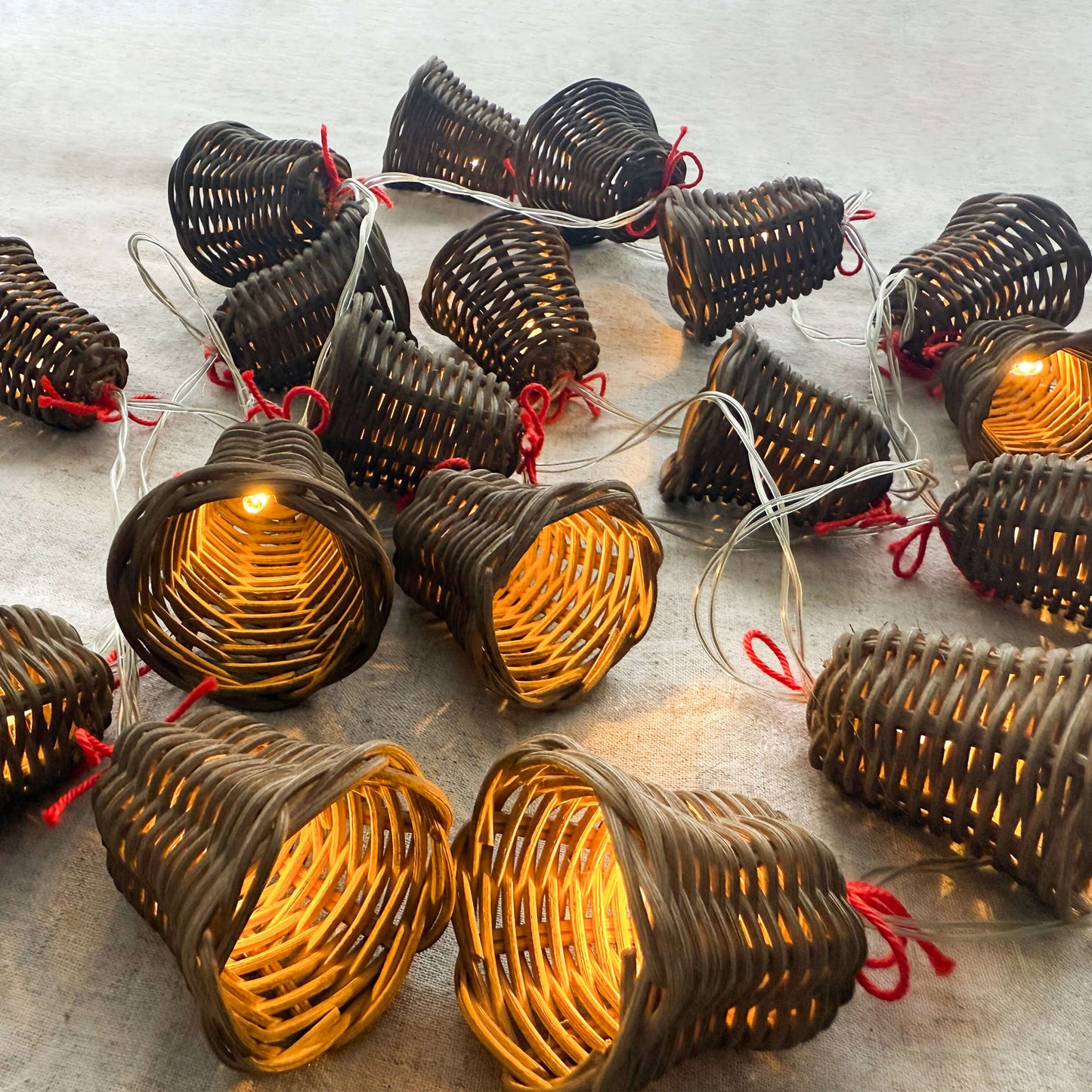 20 adet el yapımı rattan çan başlıklı LED ışık zinciri, kırmızı ip detaylı, beyaz zeminde dağınık konumda – pille çalışan dekoratif boho aydınlatma