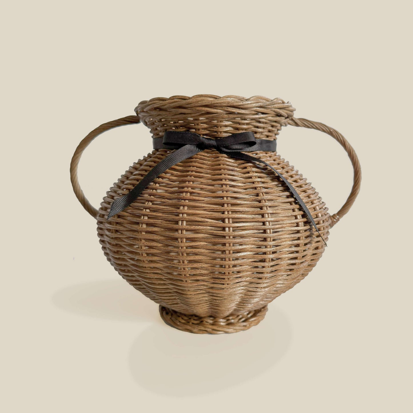 Kulplu el yapımı rattan vazo, siyah kurdele ile bağlanmış, yayvan formlu. Modern ahşap yemek masası üzerinde, kuru otlarla dekore edilmiş