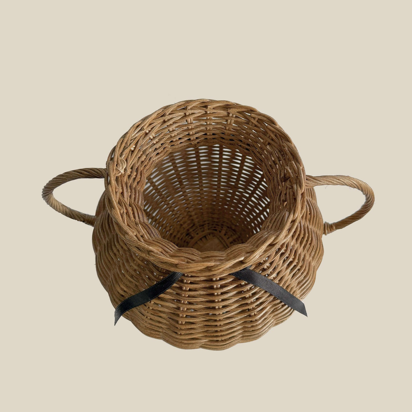 Kulplu el yapımı rattan vazo, siyah kurdele ile bağlanmış, yayvan formlu. Modern ahşap yemek masası üzerinde, kuru otlarla dekore edilmiş