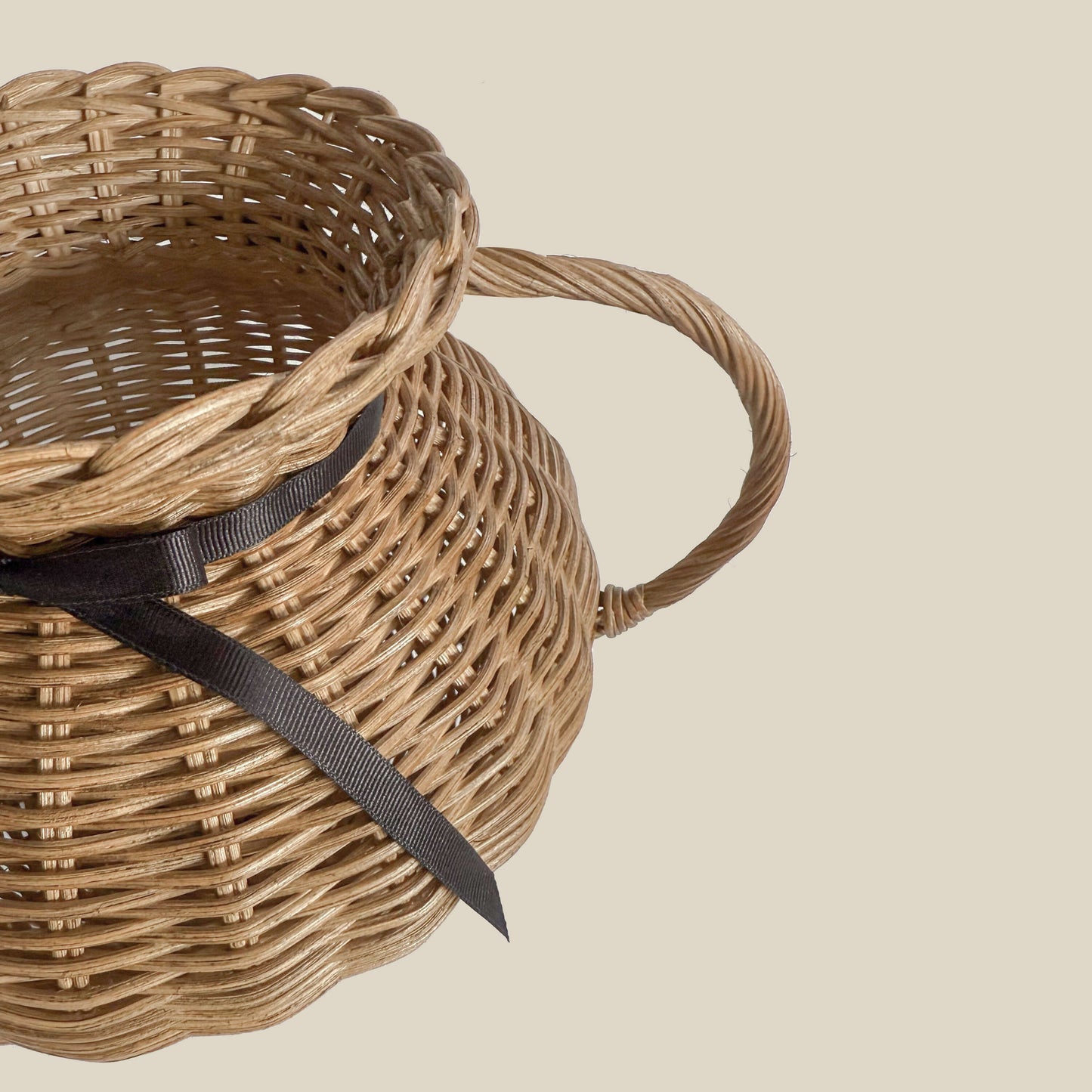 Kulplu el yapımı rattan vazo, siyah kurdele ile bağlanmış, yayvan formlu. Modern ahşap yemek masası üzerinde, kuru otlarla dekore edilmiş