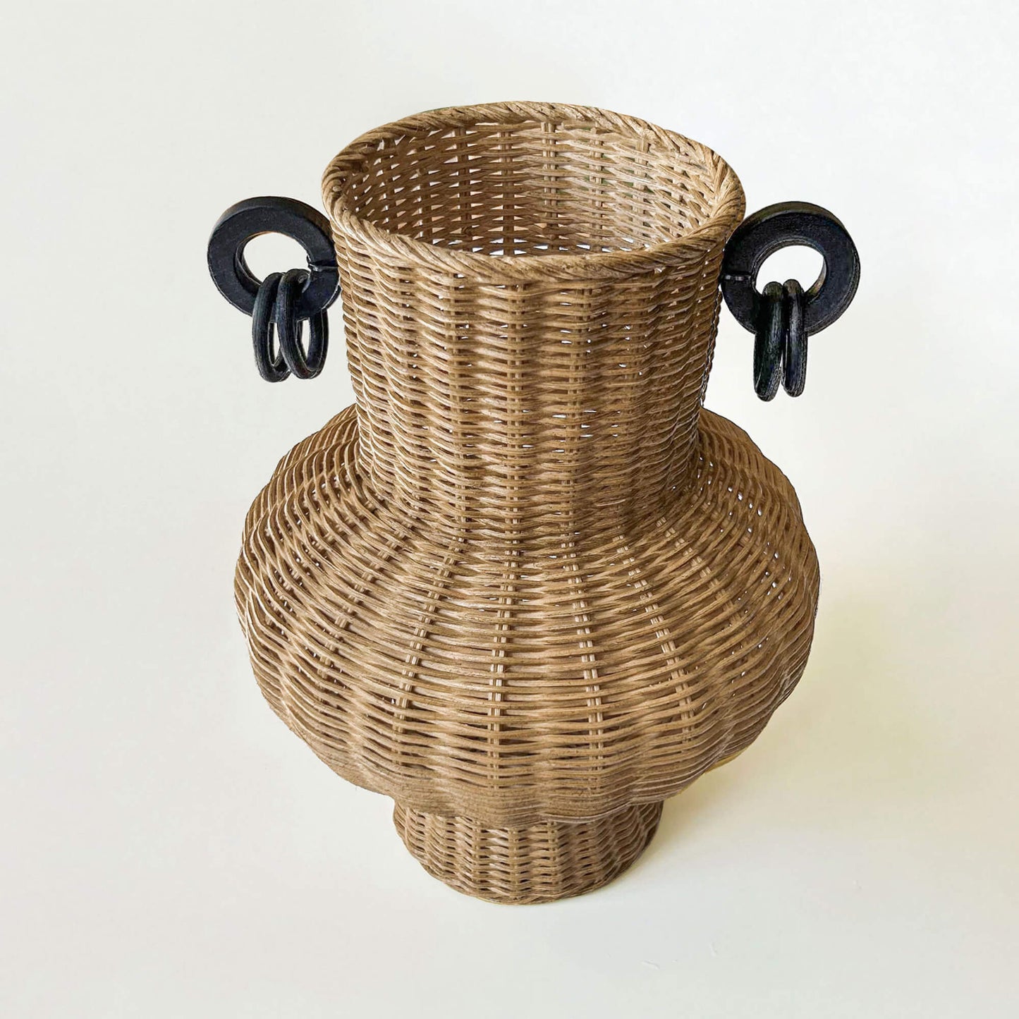 İki kulplu el yapımı rattan vazo; kurumuş dallarla dekore edilmiş, ahşap sehpa üzerinde, yanında ahşap objeler ve dekoratif kitaplarla birlikte