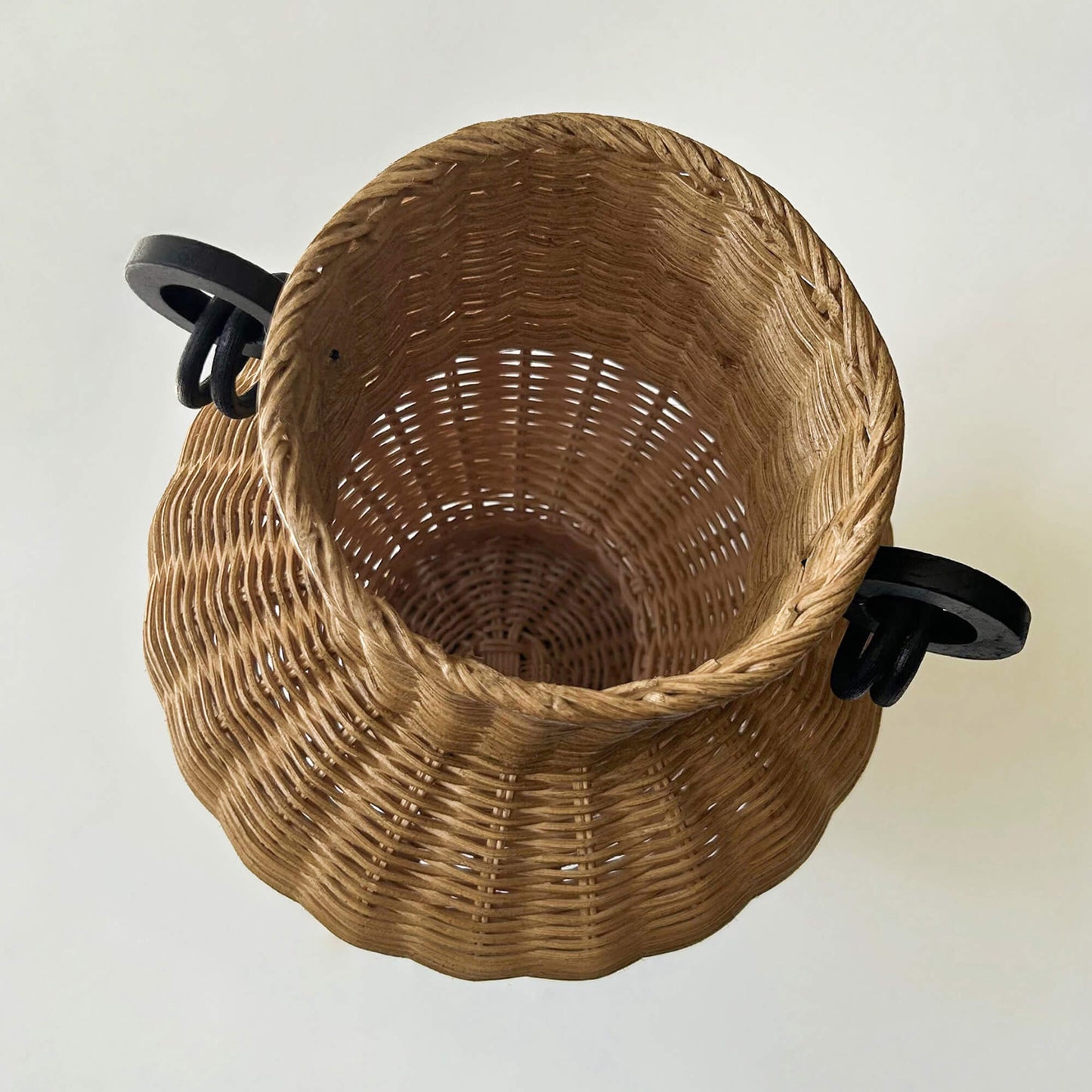 İki kulplu el yapımı rattan vazo; kurumuş dallarla dekore edilmiş, ahşap sehpa üzerinde, yanında ahşap objeler ve dekoratif kitaplarla birlikte