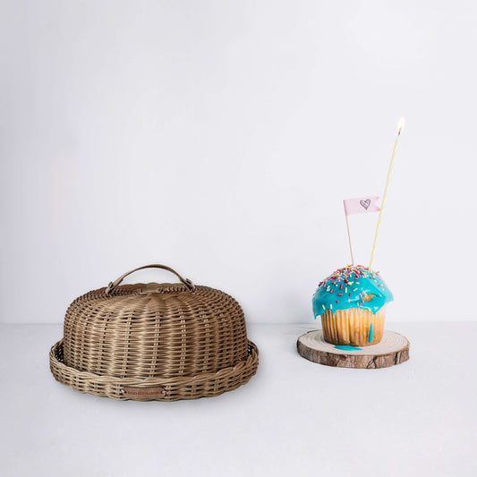 Boho tarzında dekore edilmiş bir mutfakta, el yapımı hasır ve rattan mini kek fanusu; yanında renkli cupcake ve doğal aksesuarlarla birlikte estetik bir sunum için sergileniyor